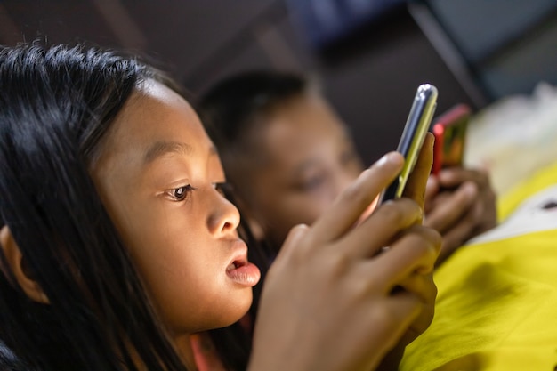 brother and sister are happily using smartphones in bed at night.