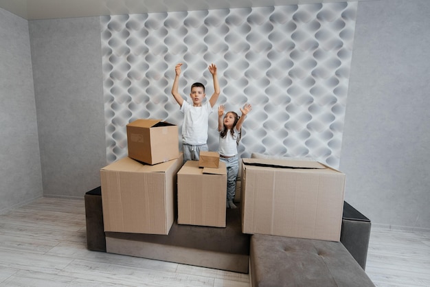 Brother and sister are playing and enjoying moving to a new apartment against the background of cardboard boxes on the couch Purchase of real estate Housewarming delivery