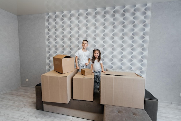 Brother and sister are playing and enjoying moving to a new apartment against the background of cardboard boxes on the couch Purchase of real estate Housewarming delivery