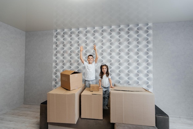 Brother and sister are playing and enjoying moving to a new apartment against the background of cardboard boxes on the couch Purchase of real estate Housewarming delivery