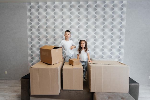 Brother and sister are playing and enjoying moving to a new apartment against the background of cardboard boxes on the couch Purchase of real estate Housewarming delivery