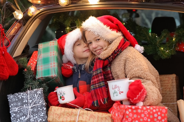 형제 자매는 많은 선물 상자가 새해로 장식된 차에 앉아 있습니다