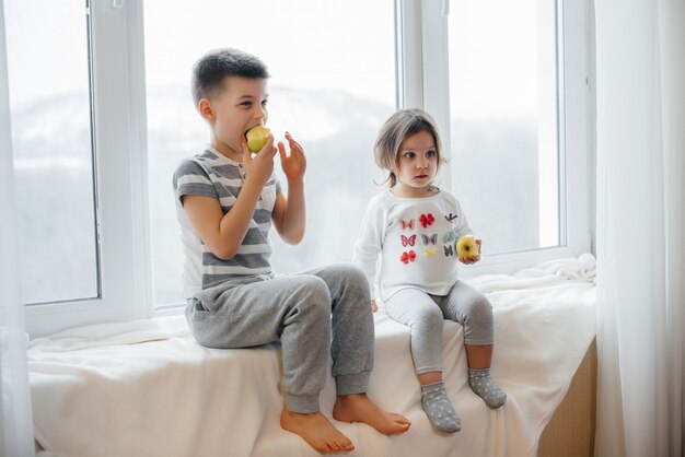 Fratello e sorella sono seduti sul davanzale a giocare e mangiare mele. felicità