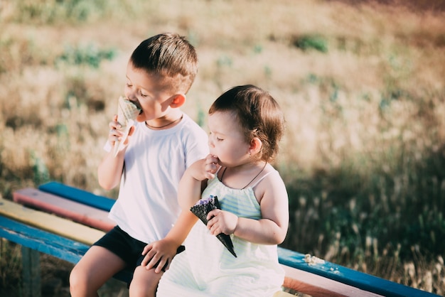 Brother and sister eating ice cream on the bench in the Playground is very cute