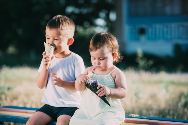 Брат и сестра едят мороженое на скамейке на детской площадке - это очень мило