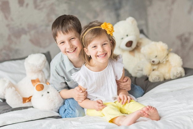 Brother and sister having fun with teddy bear in bed.