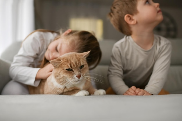 Brother and sister hugging a ginger cat on the couch