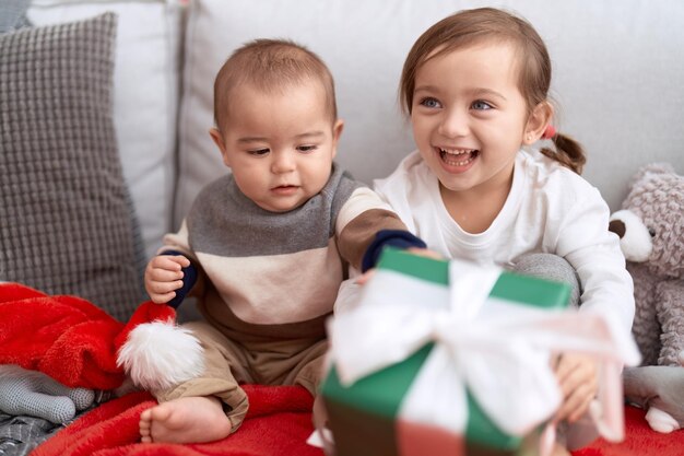 Brother and sister opening gift sitting on sofa by christmas tree at home