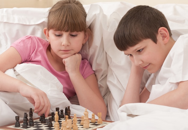 Photo brother and sister play chess in bed