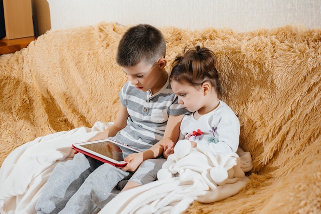 Brother and sister play on the couch in the tablet