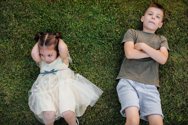 Brother and sister run, play and have fun on the grass in the park on a summer day during sunset. Happy childhood.