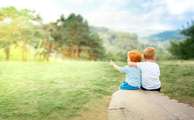 兄と妹は座って、子供と自然のリアビューの概念の風景を賞賛します