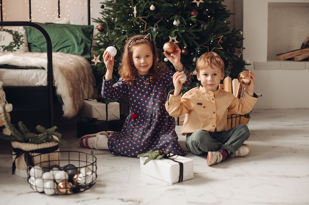 Fratello e sorella che si siedono sul pavimento con le palle di natale