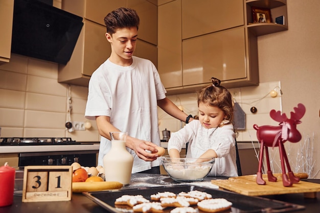 Brother with his little sister preparing food by using flour on kitchen and have fun.