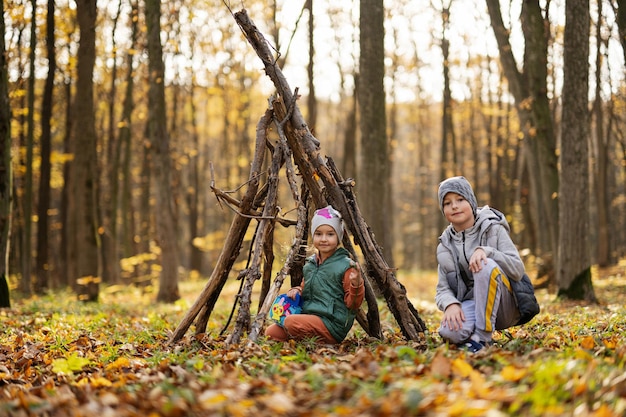 Brother with sister constructs a house from sticks in autumn forest