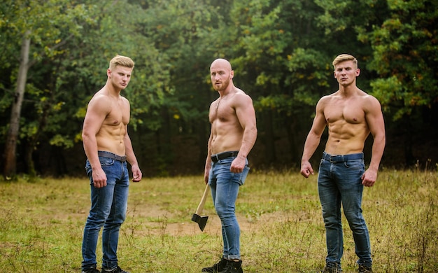 Brotherhood concept Strength and perseverance Men with muscular torso Strong men nature background Inspiring training harder Group muscular men with axe Athletic man use ax Wild masculinity