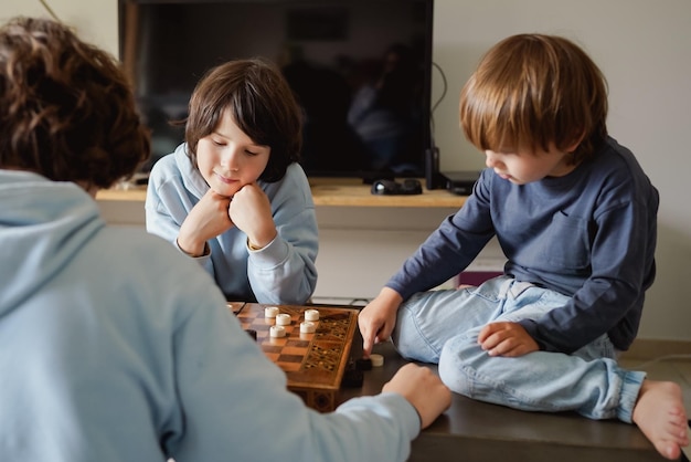 Brothers playing the checkers at home siblings playing the board strategy game spending time together