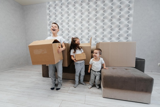 Photo brothers and sister are playing and enjoying moving to a new apartment against the background of cardboard boxes and a sofa purchase of real estate housewarming delivery