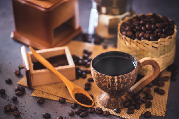 Brouw zwarte koffie in kokosnotenbeker en ochtendverlichting. Gebrande koffiebonen in een bamboemand en een houten lepel.