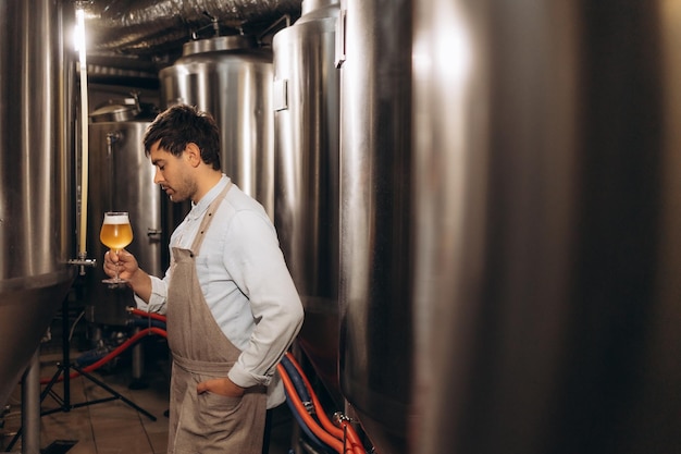 Brouwerijwerker kijkt naar vers gemaakt bier in een glazen beker