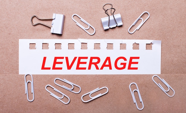 On a brown background, white paper clips and a torn strip of white paper with the text LEVERAGE