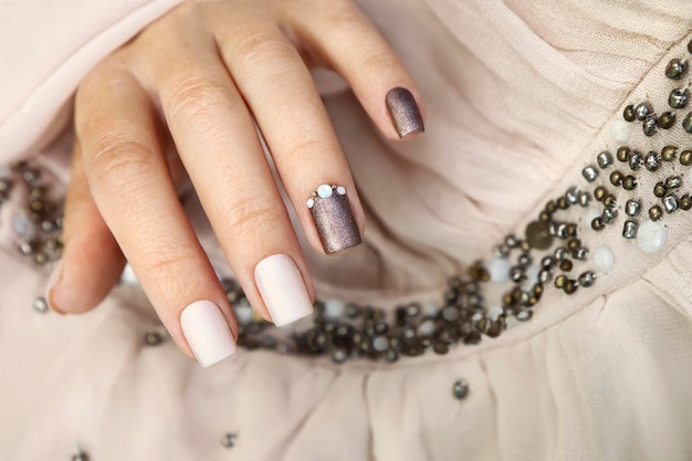 Foto manicure marrone beige con strass su unghie corte.