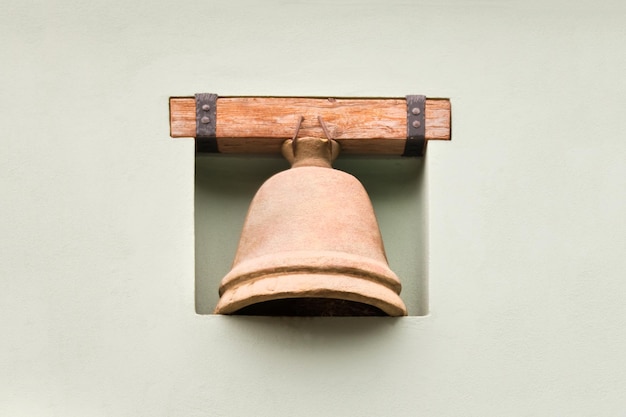 Brown bell on a wooden plank in a niche of white stone wall