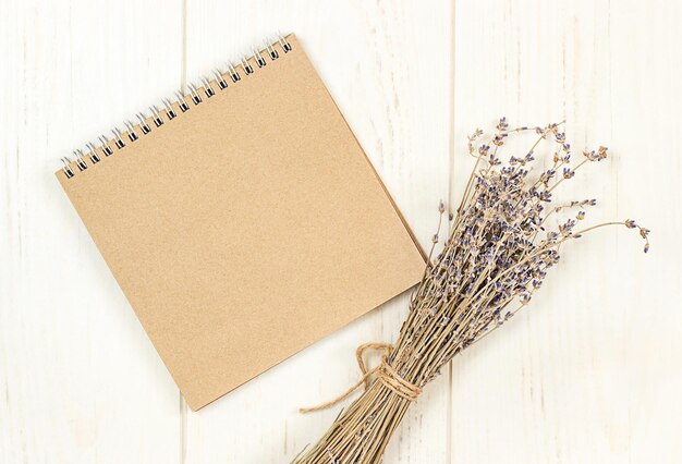brown blank notepad on white wooden background with lavender bouquet