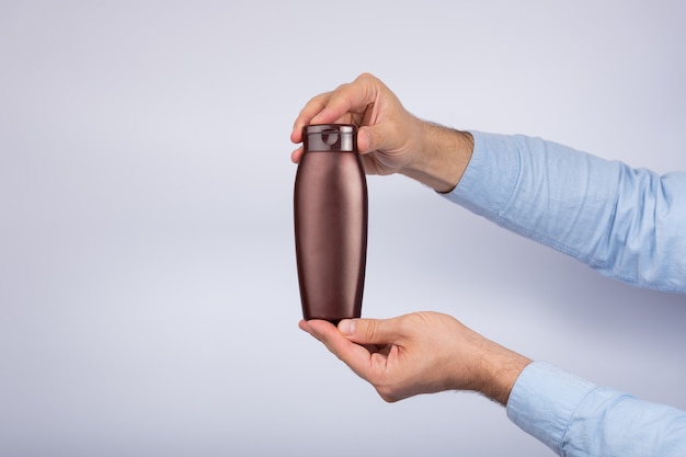 Photo brown bottle of shampoo or lotion in male hand on white