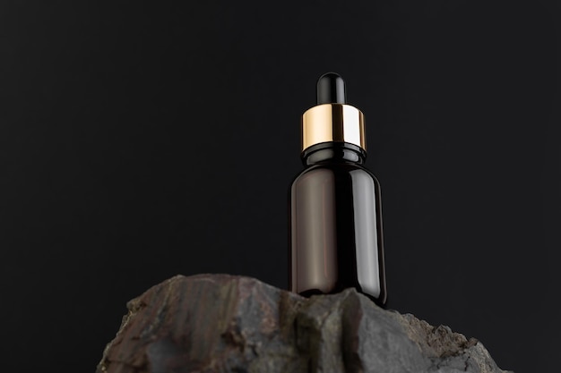 Brown bottle with dropper with a beauty serum on a granite stone on black background Glass packaging for cosmetic product essential aroma oil Skin care hydration and nutrition with collagen