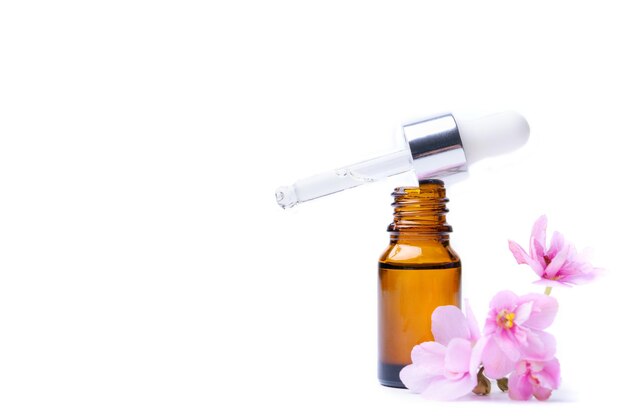 Brown bottle with essential oil and pink violet flower on a white background copy space