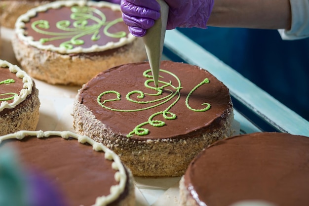 Brown cakes with green ornament. Worker's hand decorating a cake. Putting cream on cake's surface. Standard of quality.