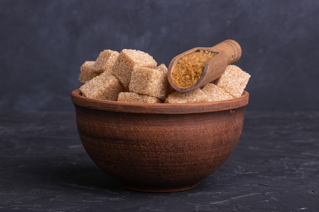 Brown cane sugar cubes in a clay bowl with a wooden spoon