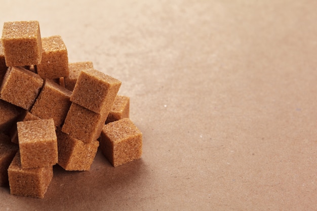 Cubi dello zucchero di canna di brown su un marrone chiaro