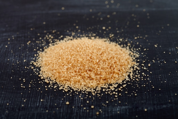 Brown cane sugar heap on black board.