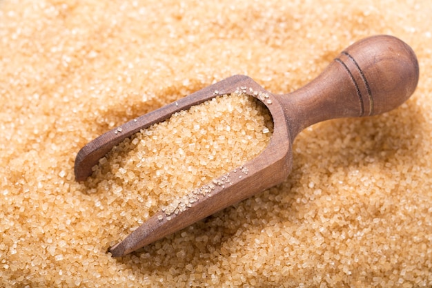 Brown cane sugar with wooden scoop as background