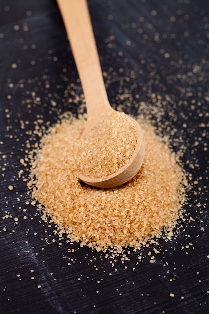 Brown cane sugar in wooden spoon on black board.