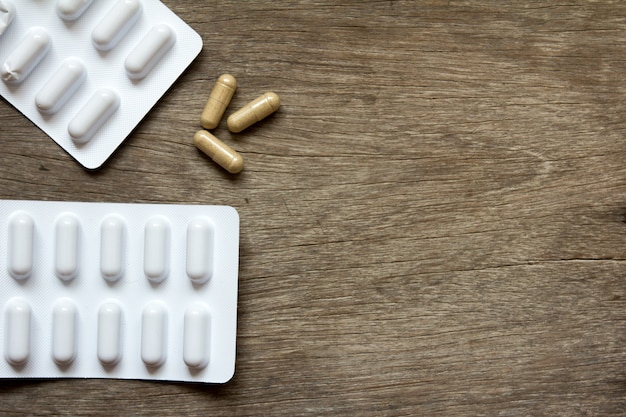 Brown capsule and white blister on wooden background