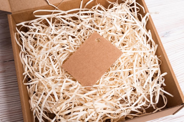 Brown carton, cardboard box with filler and tag on wooden desk