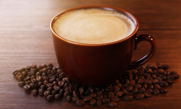 Brown ceramic cup of coffee decorated with roasted beans around on wooden background close up