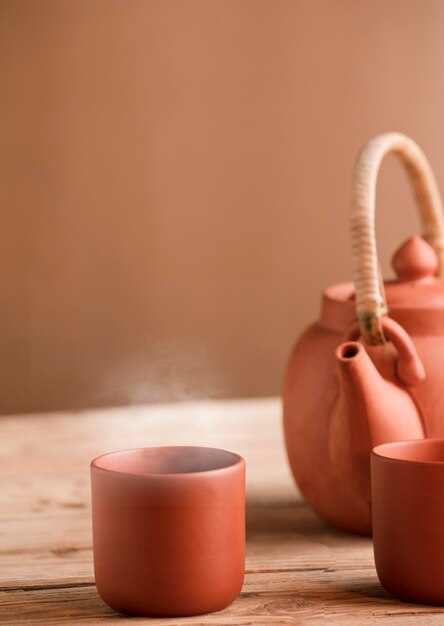 Brown ceramic mug with tea or coffee and hot steam on rustic wooden table partial view of teapot