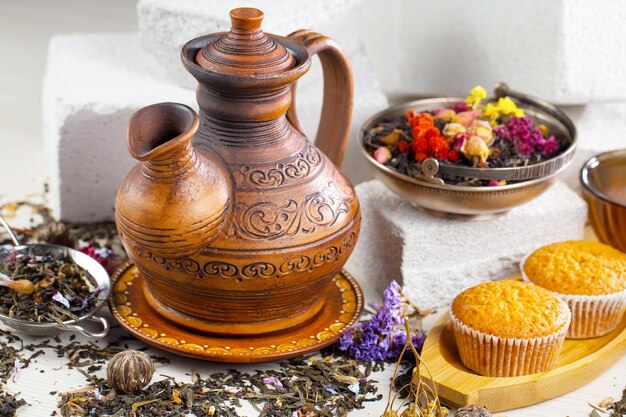 A brown ceramic teapot with a cup of tea on a table with a cake in the background.