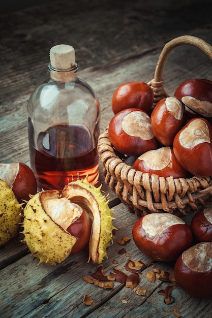 Brown chestnuts in basket and bottle of healthy tincture on old wooden table Retro styled