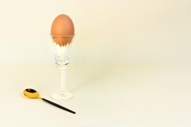 Photo brown chicken egg in crystal glass with golden black spoon beige background copy space easter spring holiday concept minimal style festive food composition modern creative social media advertisement