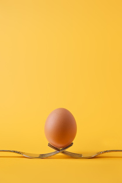 Brown chicken egg standing on two crossed forks on yellow