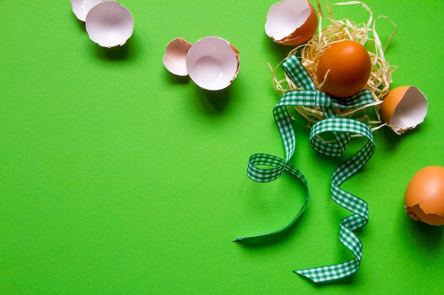 Brown chicken egg in a straw nest, broken eggshell and green checkered ribbon