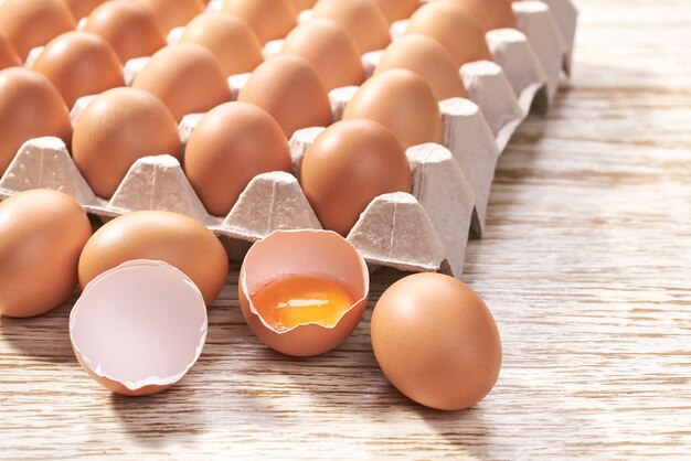 Brown chicken eggs in a cardboard tray close up on a white wooden table.