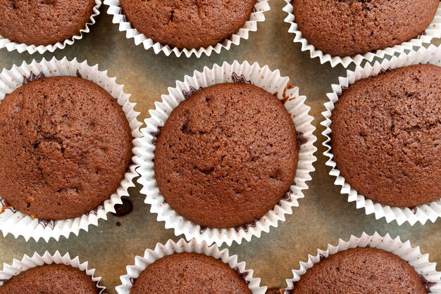 Foto muffin al cioccolato marrone avvolti in carta bianca cotti nel forno sdraiati su carta da forno vista dall'alto