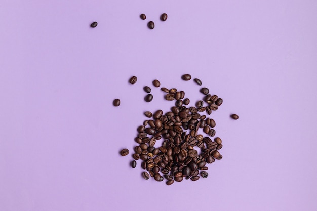 Brown coffee beans heap on purple background with copy space.