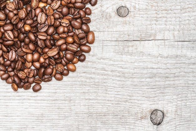 Brown coffee beans on light color wood background. Copy space. Close-up macro top view of still life.